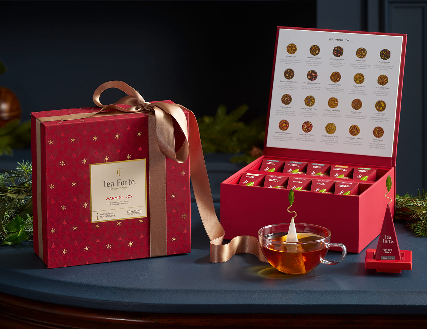 Warming Joy Tea Chest, one wrapped with a ribbon, the other open, with a glass teacup and infuser on a red tray