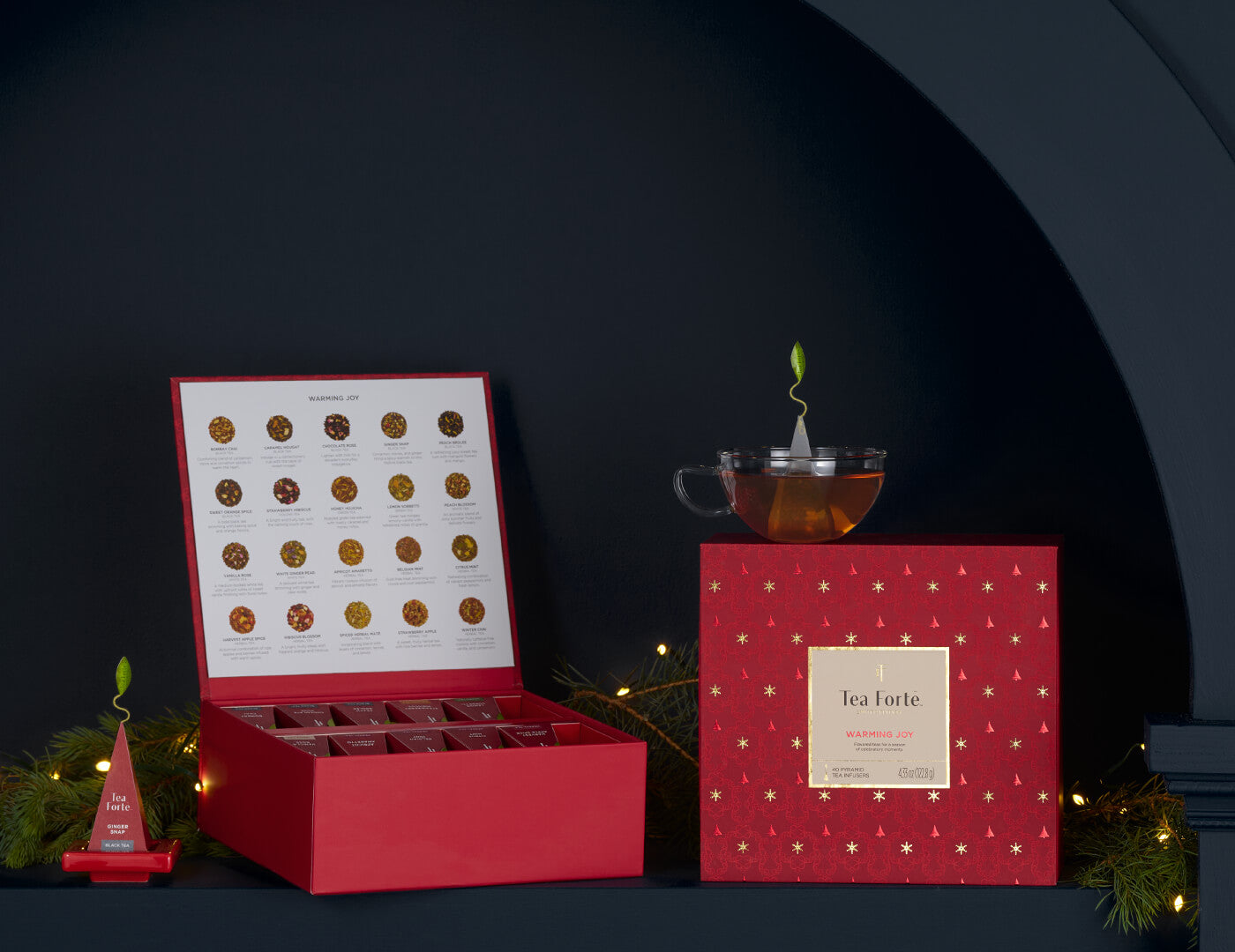 Warming Joy Tea Chest, one closed, the other open, with a glass teacup and infuser on a red tray on a shelf
