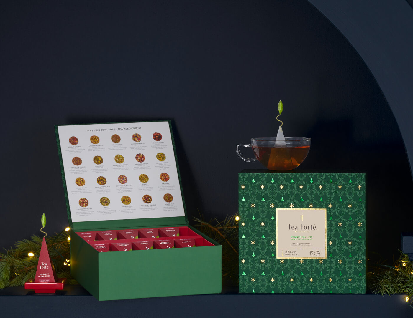 Warming Joy Tea Chest, one closed, the other open, with a glass teacup and infuser on a red tray on a dark shelf