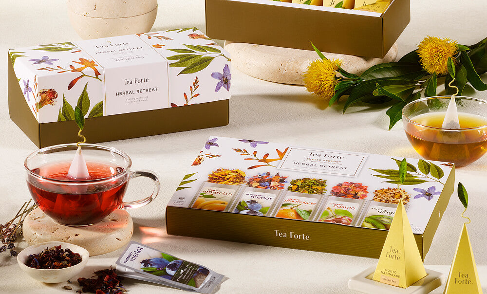 Herbal Retreat tea assortment in a 20 count Presentation Box on table with teacups, teapot and pouches of loose leaf tea.